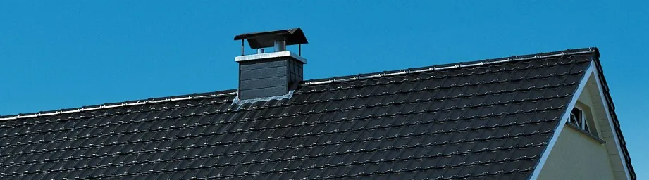 Dunkel gedecktes Steildach mit Schornstein vor blauem Himmel